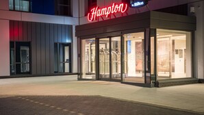 Esterno di un hotel Hampton di notte, con ingresso in vetro e insegna al neon.
