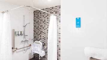 Un baño moderno con ducha, barras de apoyo y una toalla blanca sobre un tapete de madera.