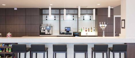 A modern bar area with a white countertop, dark wooden cabinets, and bar stools.