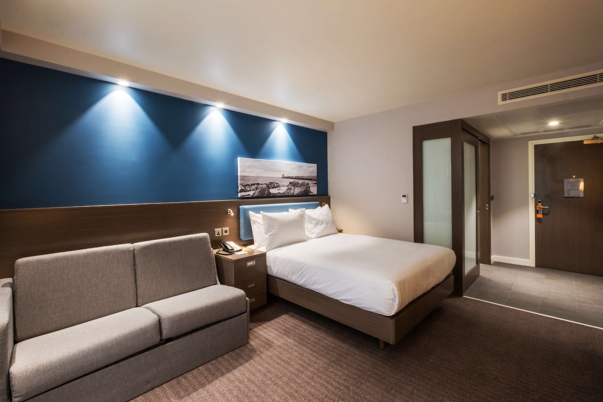 A hotel room with a bed, a sofa, a nightstand, and a wall-mounted picture.