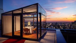 A modern glass-enclosed dining area with a city view at sunset.