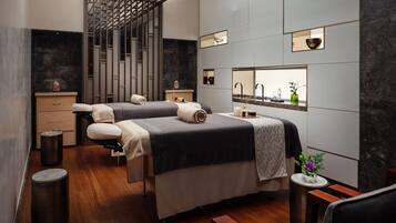Un moderno cuarto de spa con dos camillas, un lavamanos pequeño y un espejo.