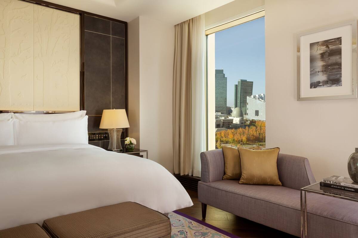 Ein Hotelzimmer mit einem großen Bett, einer Couch, einem Couchtisch und Blick auf die Stadtlandschaft.