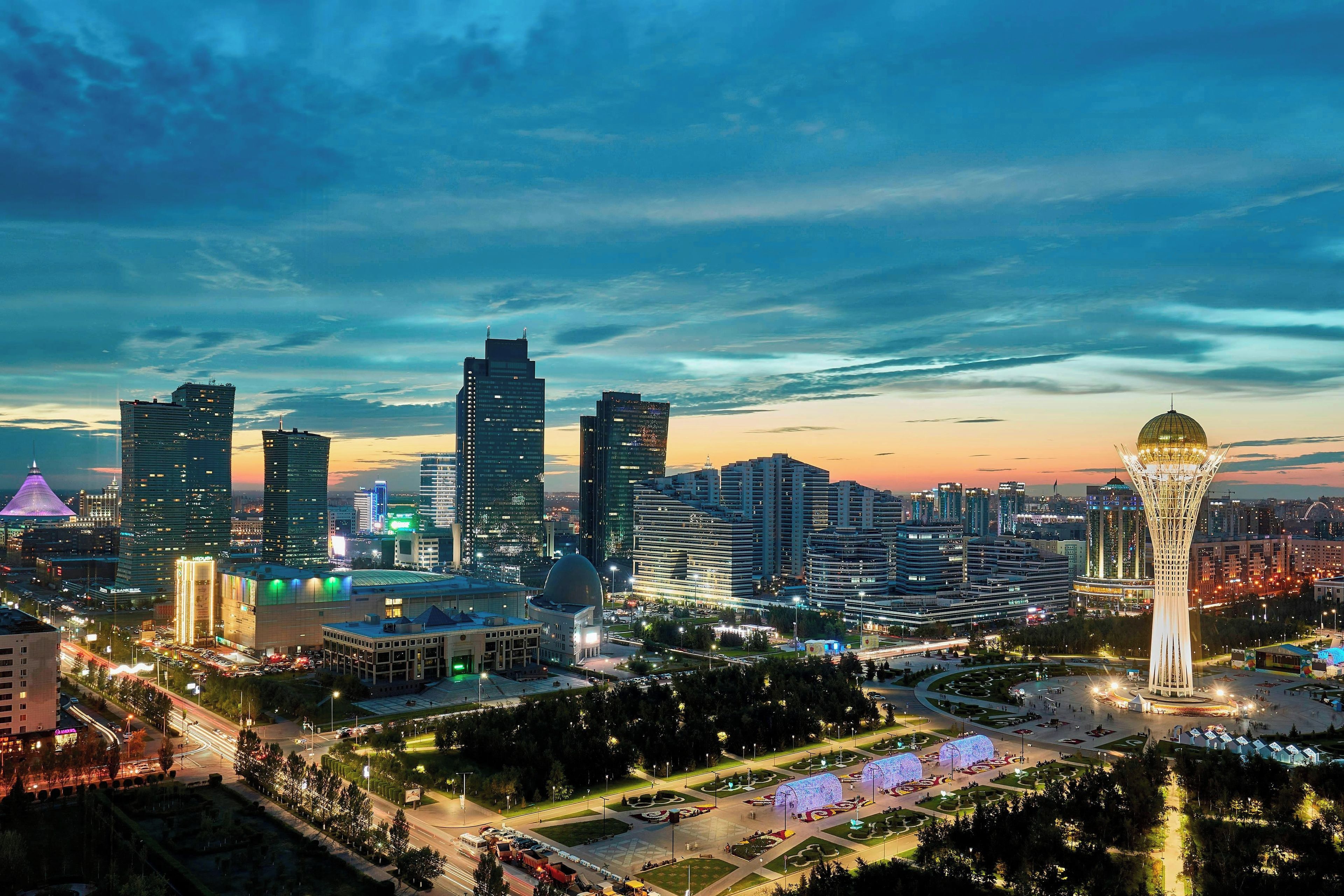 A cityscape with modern buildings, a distinctive tower, and a well-lit square.