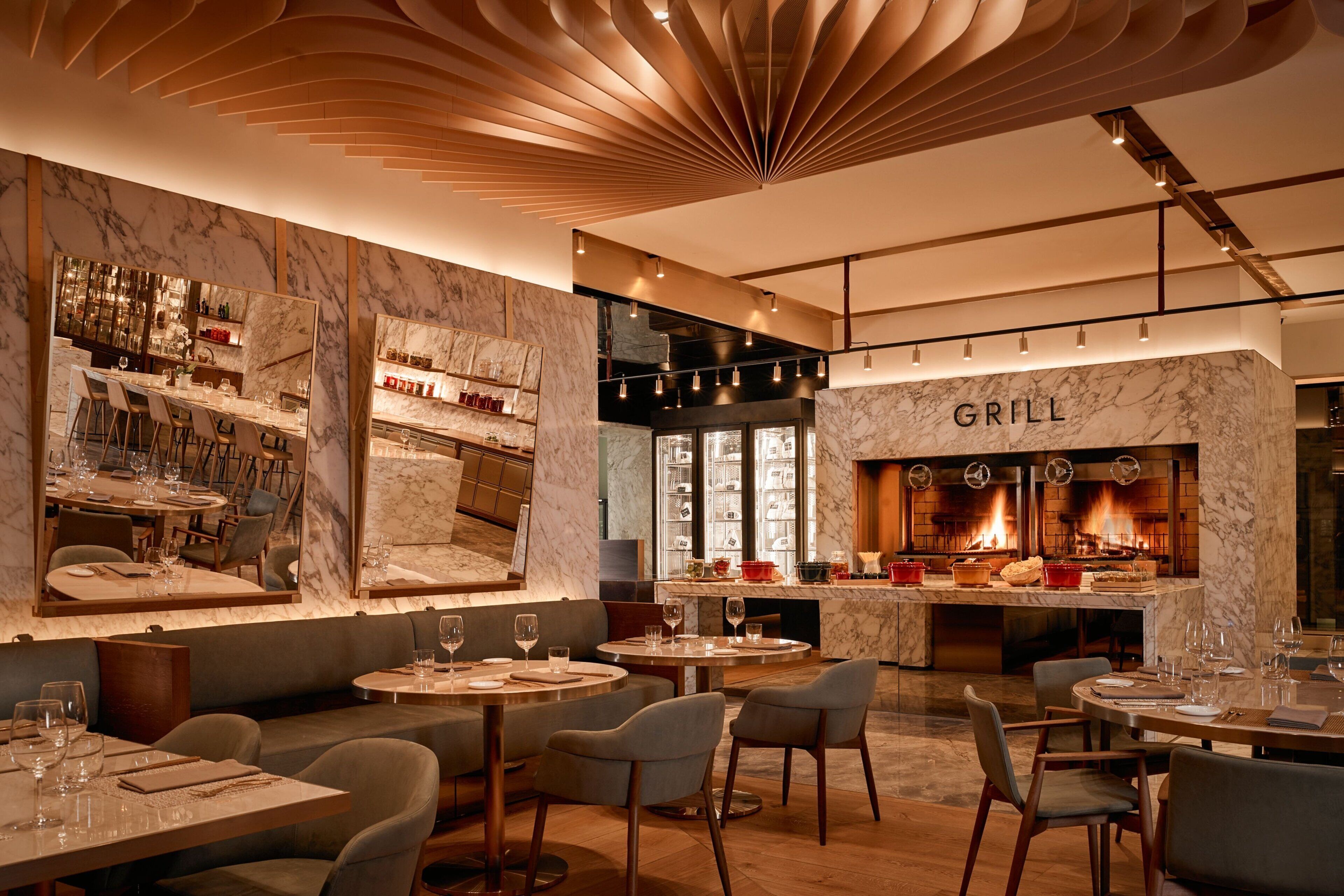 A modern restaurant with a marble bar, seating areas, and a visible grill.