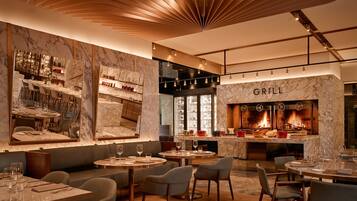 A modern restaurant with a marble bar, seating areas, and a visible grill.