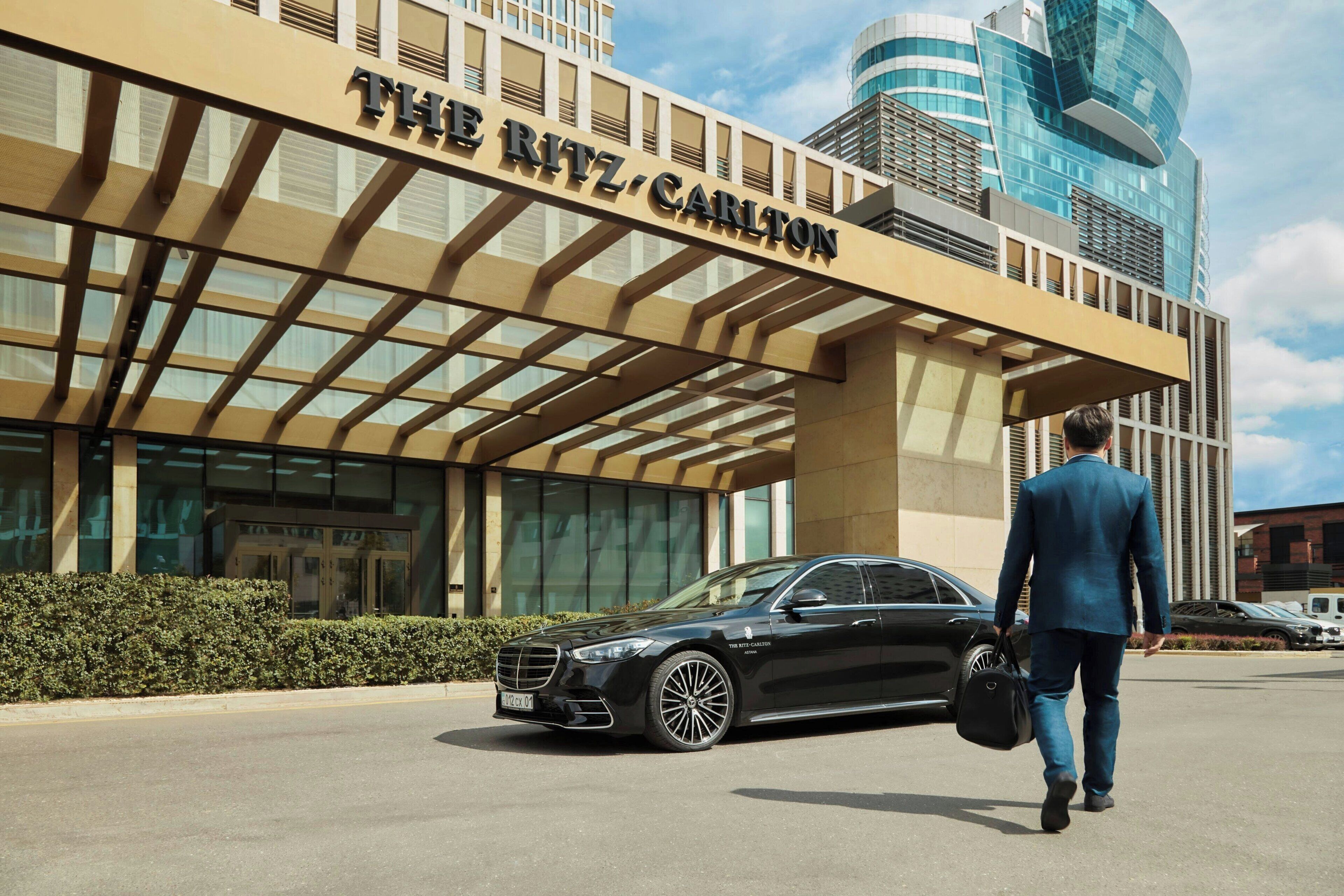 A man in a suit walking towards a black car parked in front of The Ritz Carlton hotel.