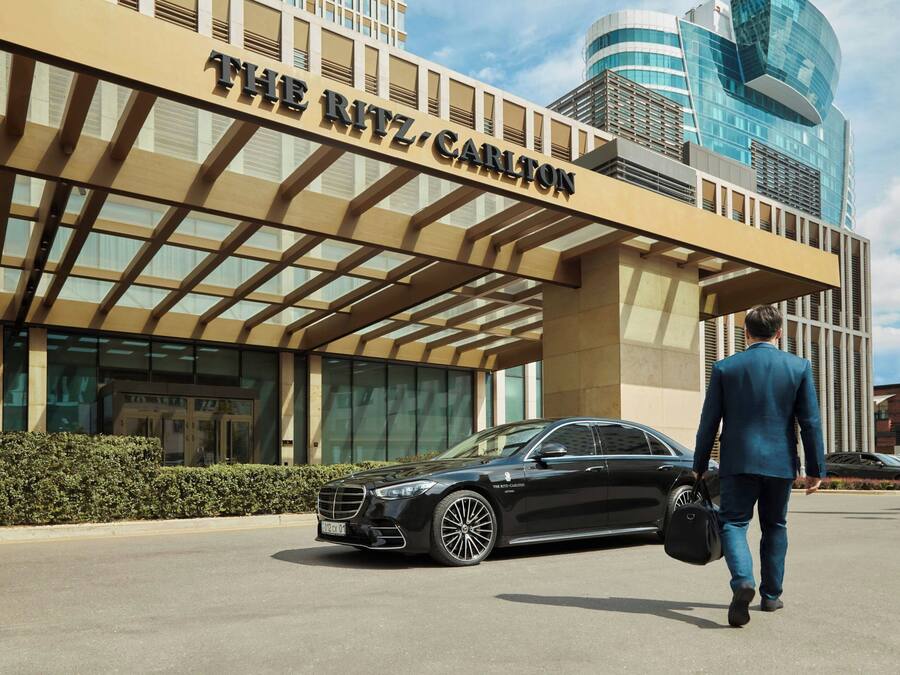 A man in a suit walking towards a black car parked in front of The Ritz Carlton hotel.