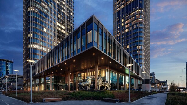 A modern building with a glass facade, large windows, and a central entrance with a sculpture.