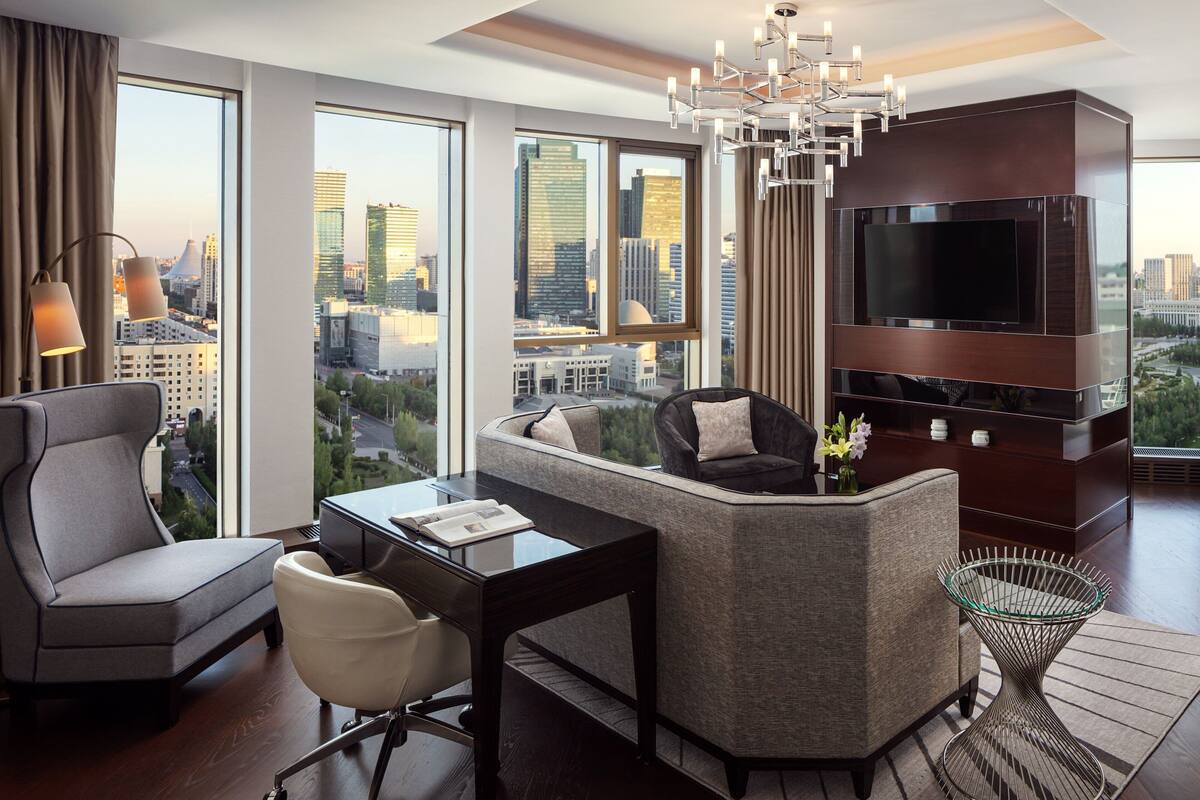 Ein modernes Hotelzimmer mit großem Fernseher, einer Couch, einem Schreibtisch und Blick auf die Stadtlandschaft.