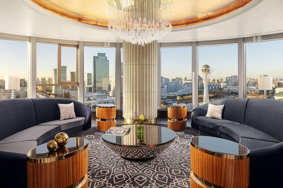 Ein modernes Wohnzimmer mit Stadtblick, das eine große Kronleuchter, zwei Sofas, einen runden Couchtisch und Holznachttische zeigt.