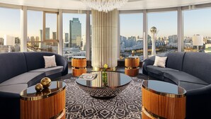 A modern living room with a city view, featuring a large chandelier, two sofas, a round coffee table, and wooden side tables.