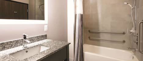 A bathroom with a granite sink, a mirror, a shower with grab bars, and a bathtub.