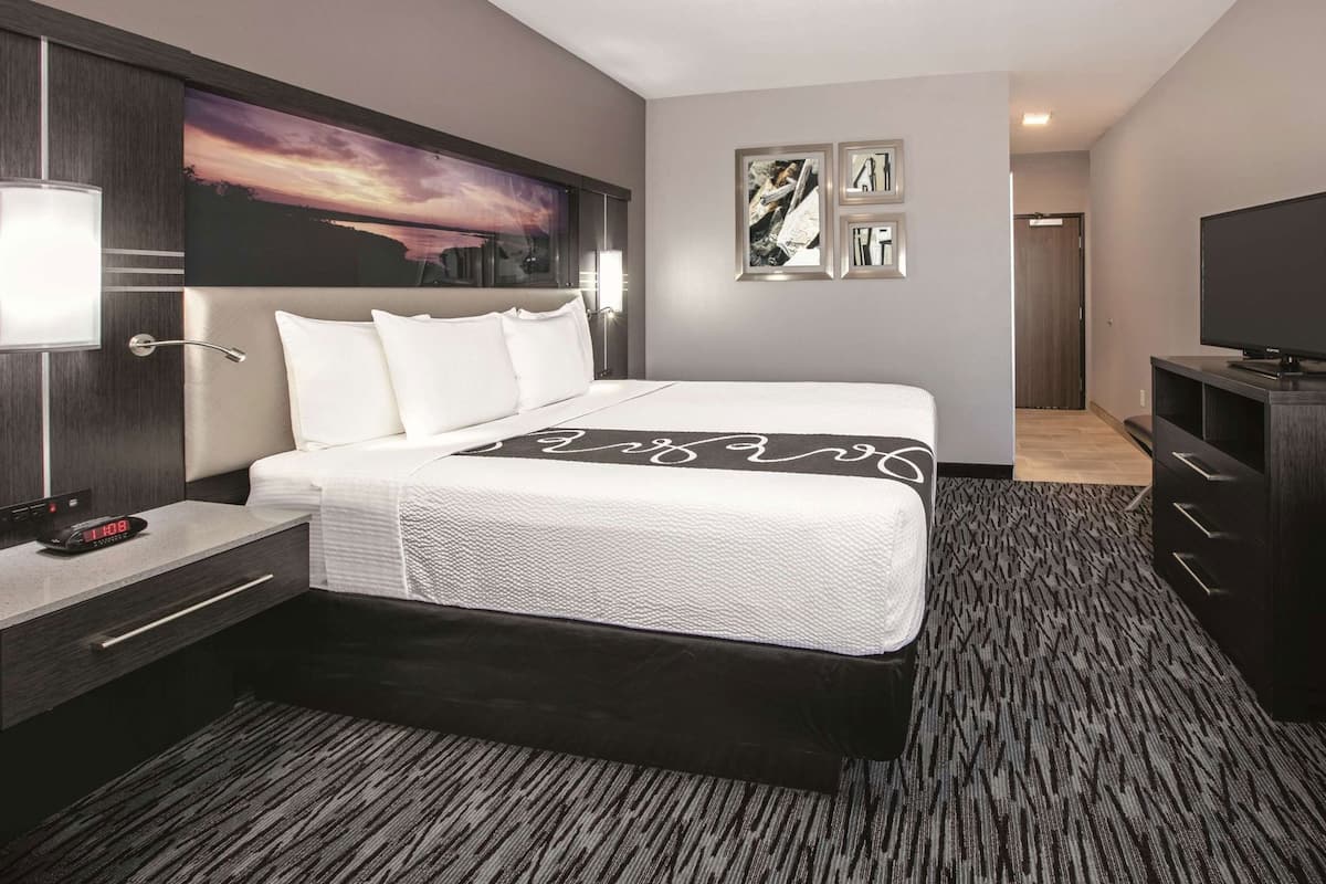 Een hotelkamer met een bed, nachtkastje, lamp, kunstwerk en een televisie.