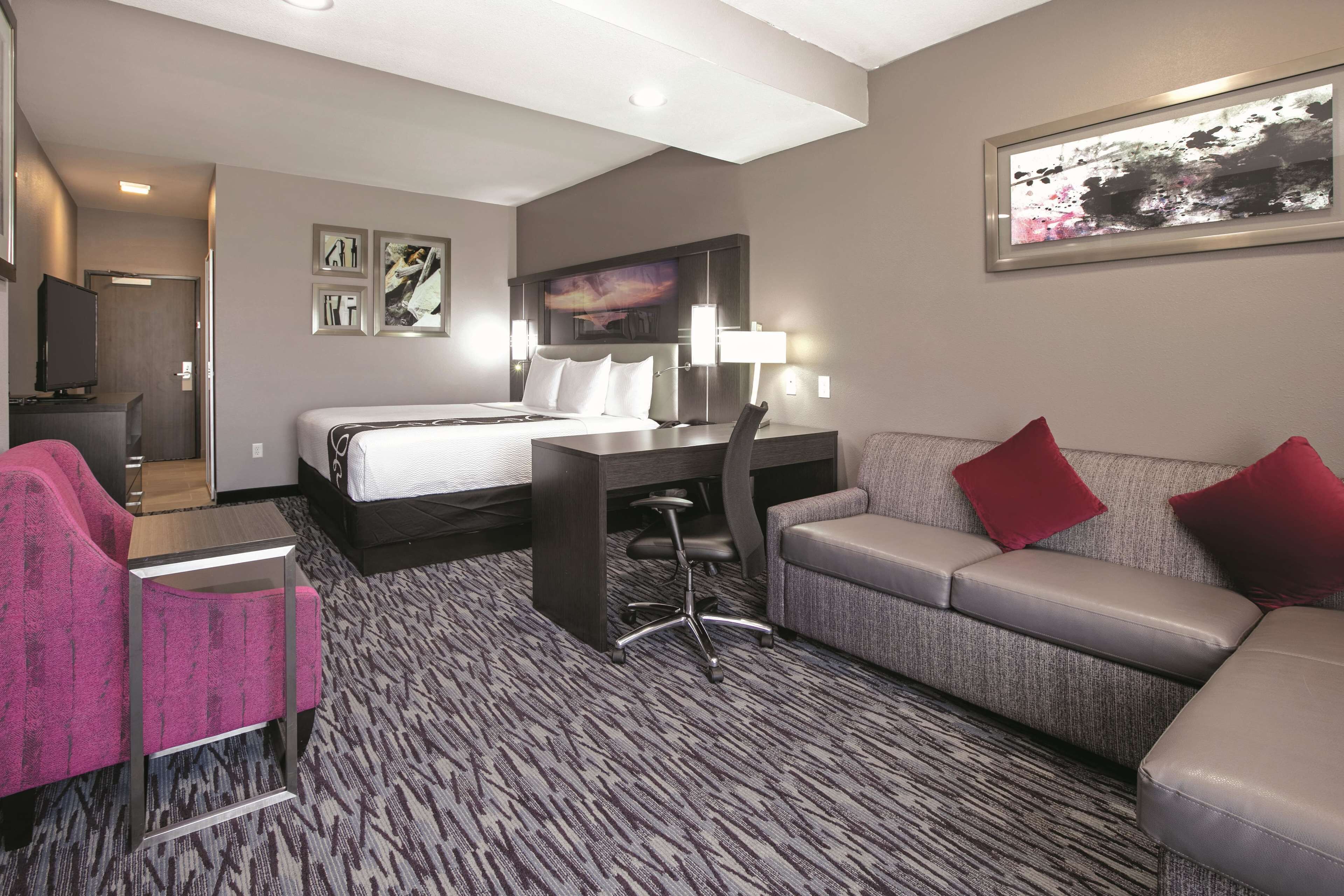 A hotel room with a bed, a desk, a chair, a sofa, and a TV.