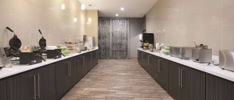 A modern kitchen with a long counter, overhead lighting, and a tiled backsplash.