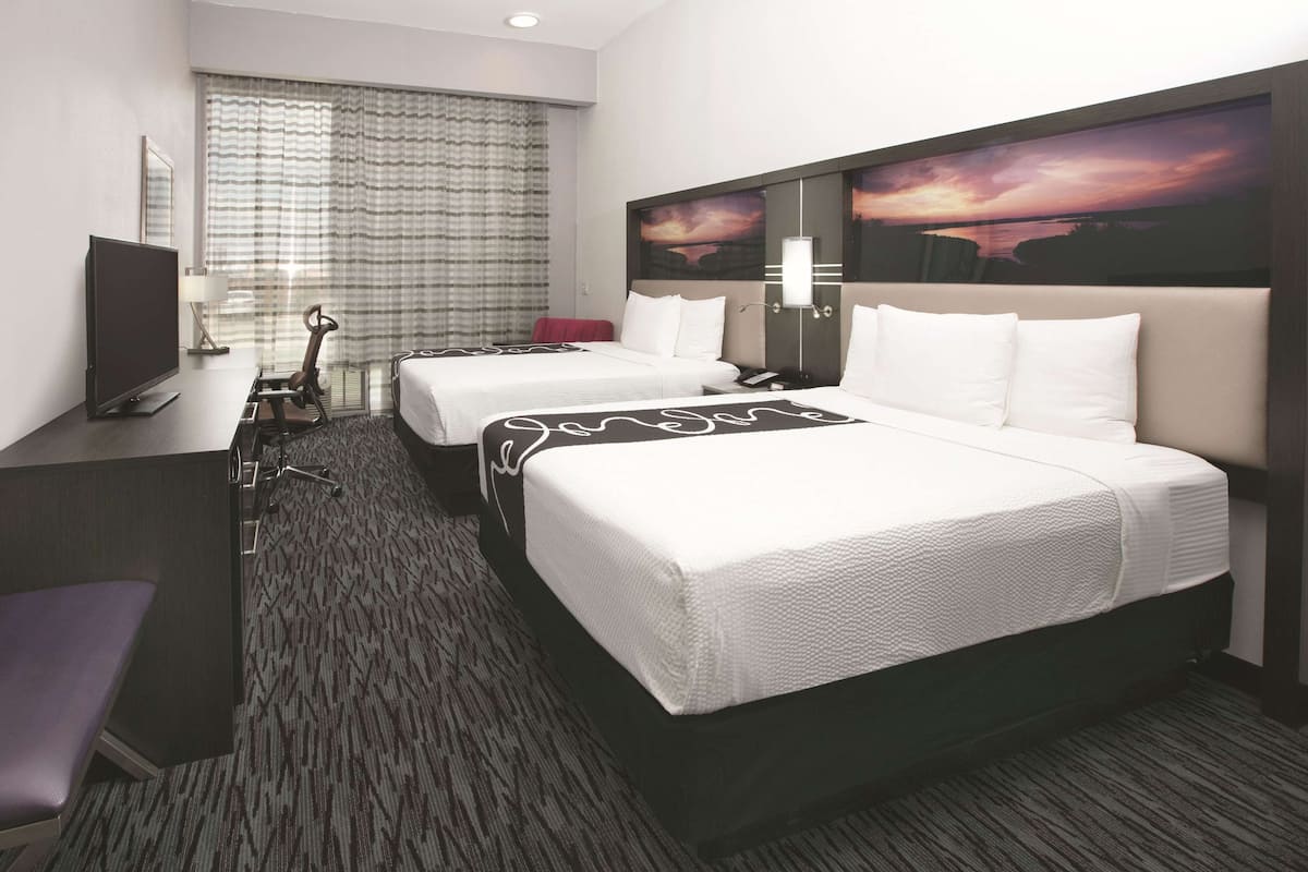 Een hotelkamer met twee bedden, een bureau, een televisie en een groot raam met gordijnen.