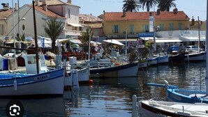 A marina with boats docked, buildings with red-tiled roofs, and palm trees in the background. - Holiday Home in Carqueiranne by the Sea (Carqueiranne)