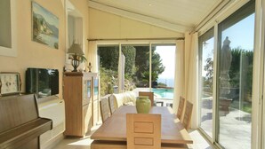 A spacious dining area with a large table and chairs, a piano, and a view of a swimming pool and landscape. - Holiday Home in Carqueiranne by the Sea (Carqueiranne)