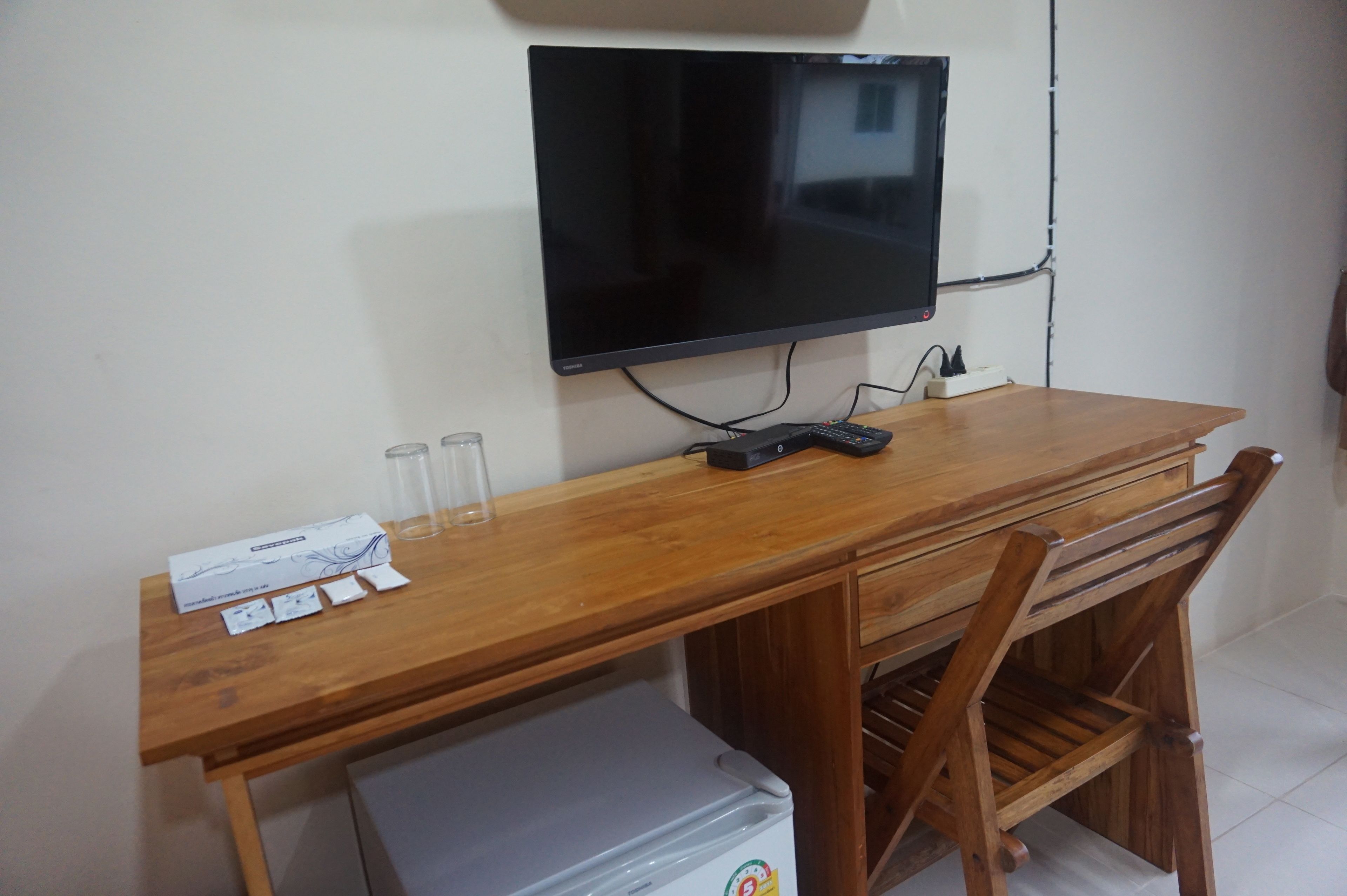 A wooden desk with a flat-screen TV, a remote control, and a small refrigerator.
