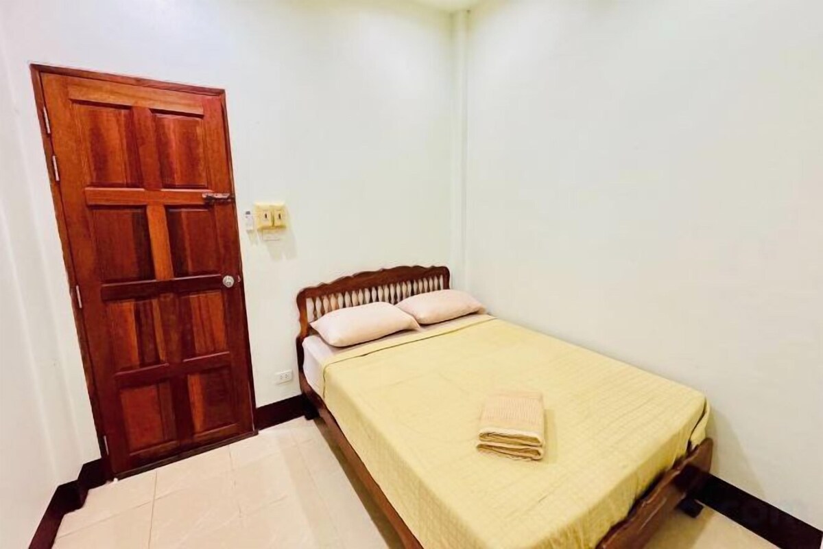 A small room with a wooden door, a bed with a yellow bedspread, and a white wall.