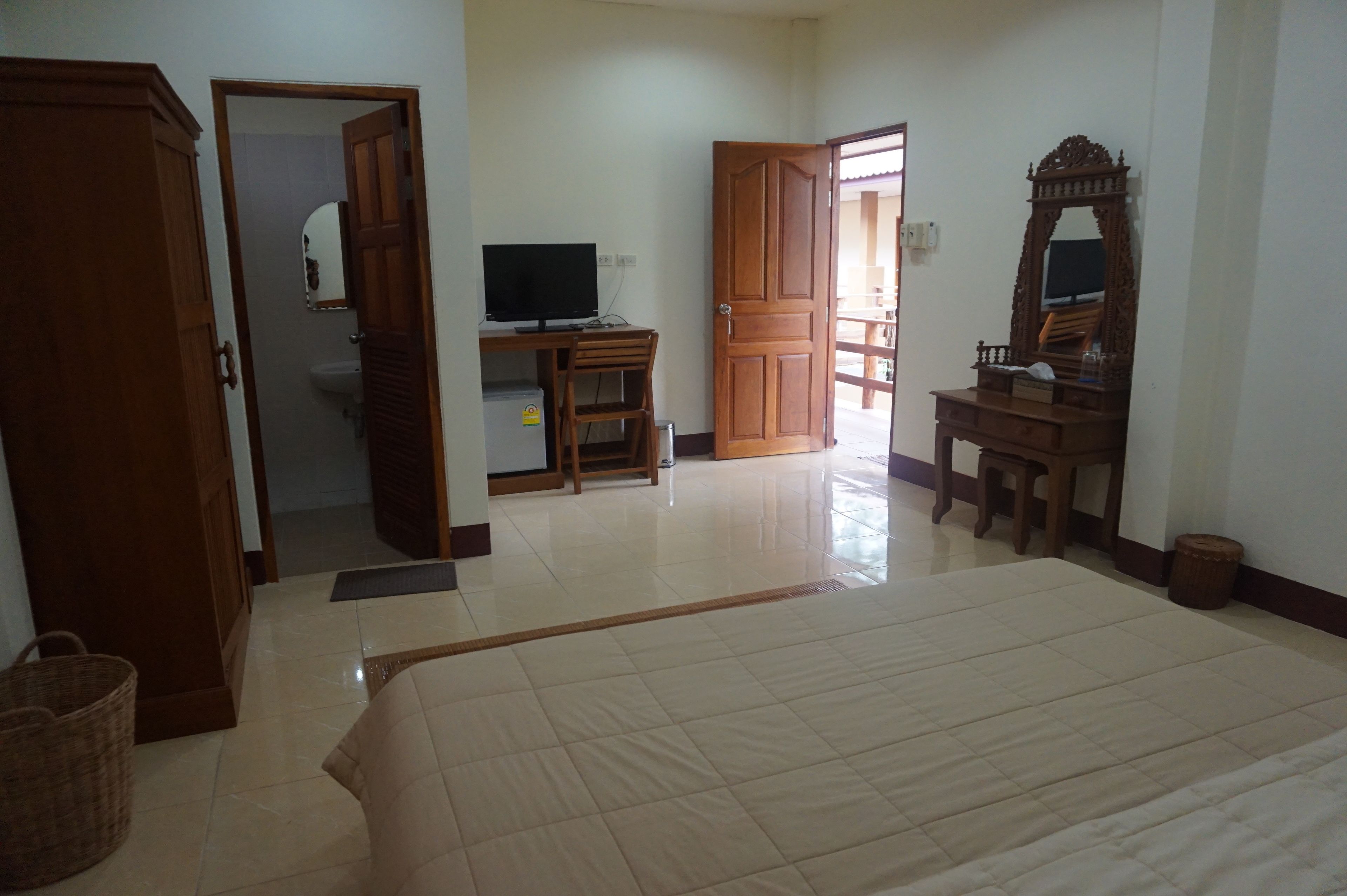 Quarto com cama, escrivaninha de madeira com televisão, espelho e guarda-roupa.