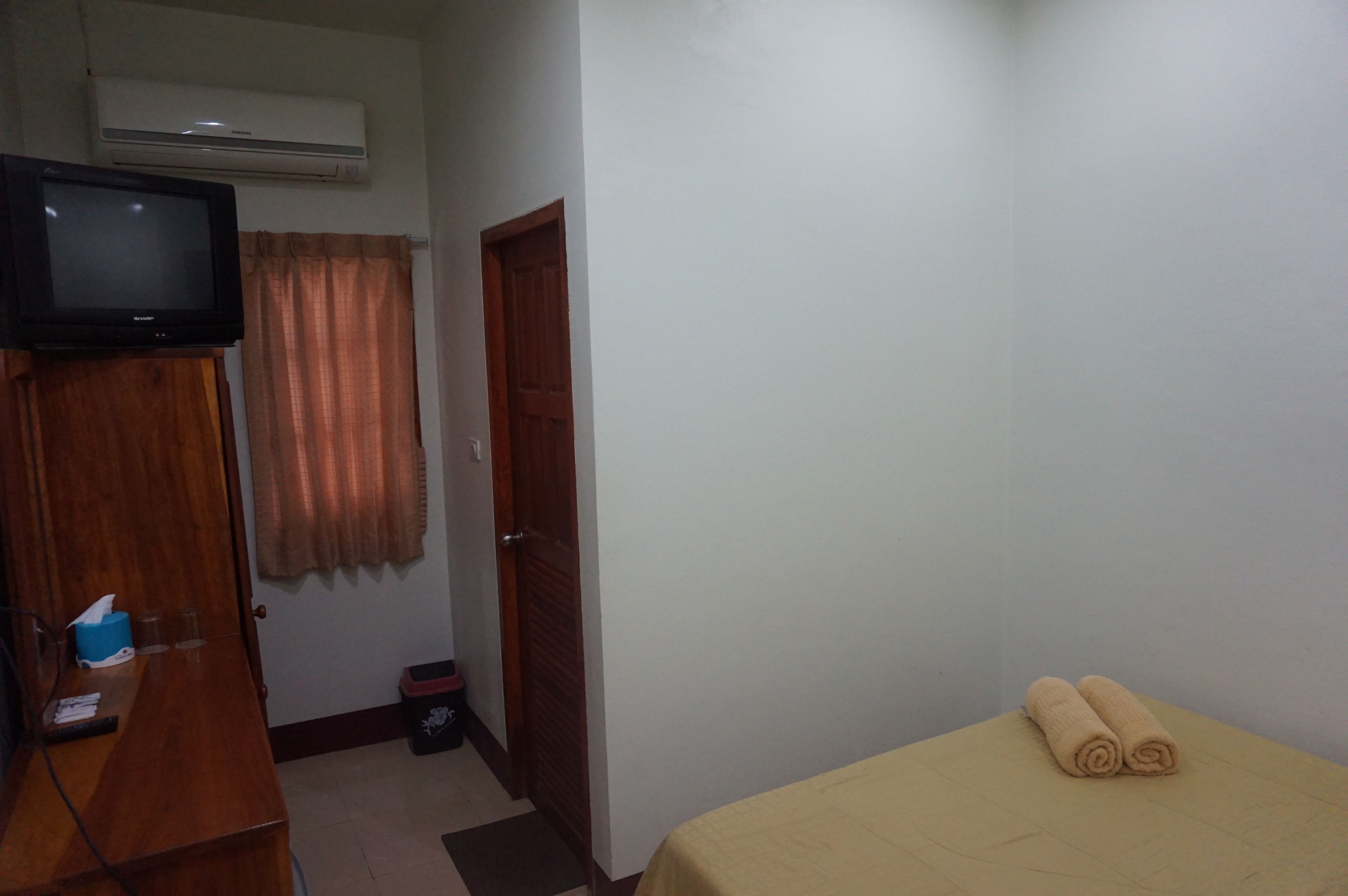 A small room with a bed, a wooden desk, a television, and a door.
