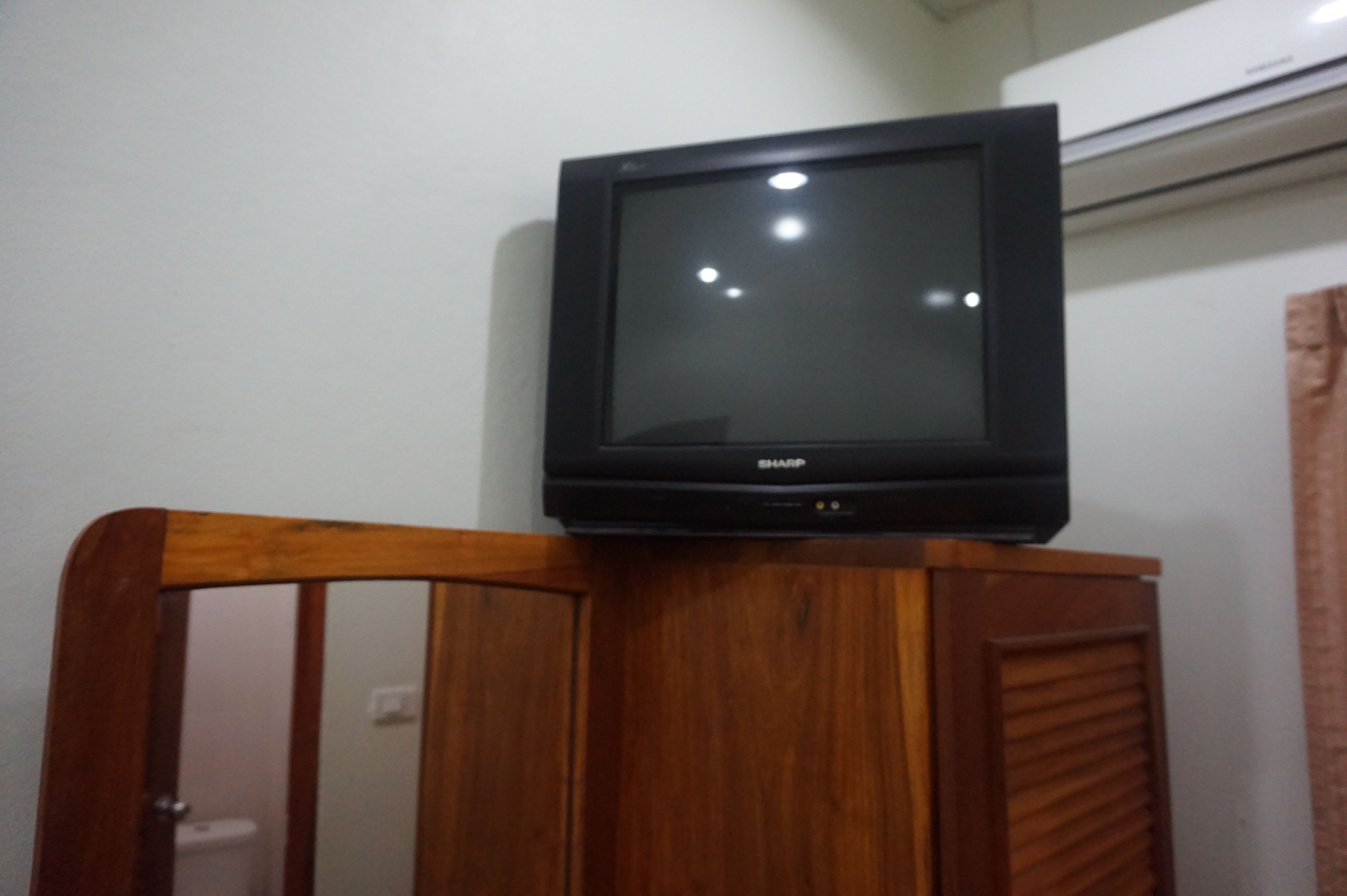 Un televisor sobre un mueble de madera en una habitación con pared blanca y un aire acondicionado.