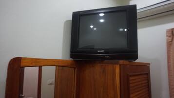 Un televisor sobre un mueble de madera en una habitación con pared blanca y un aire acondicionado.