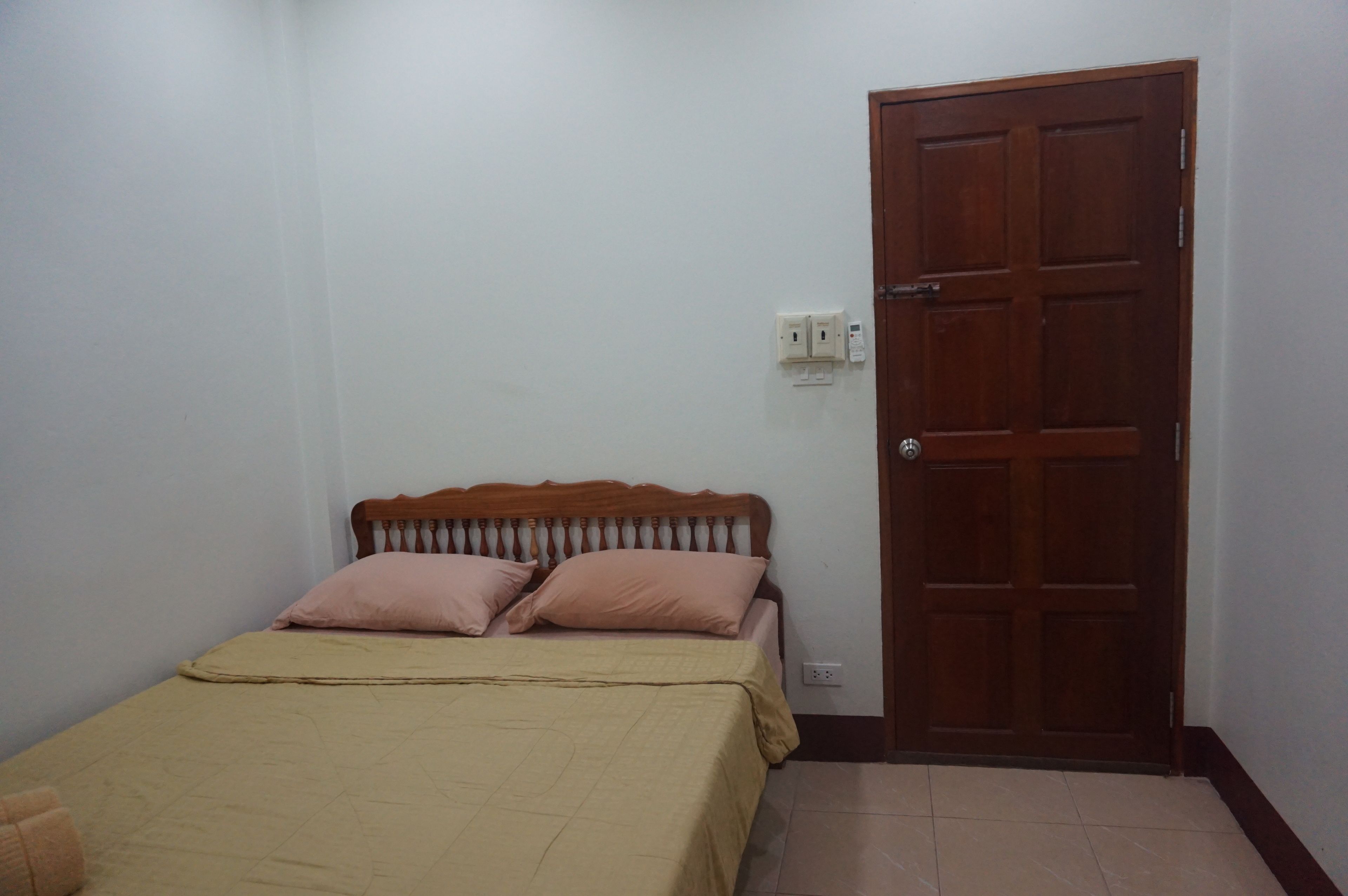 Un dormitorio con cama, dos almohadas, una puerta de madera y un enchufe.