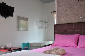 A hotel room with a bed, a TV mounted on the wall, a small table with a chair, and a window with curtains.