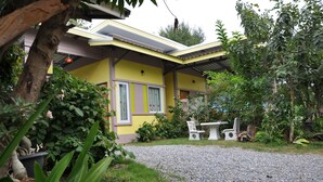 A yellow building with a covered patio area, surrounded by greenery and potted plants. - Feel Good Resort (Nakhon Ratchasima)