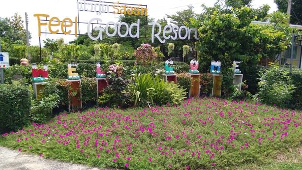 A sign for 'Feel Good Resort' with a garden in front featuring various sculptures and pink flowers. - Feel Good Resort (Nakhon Ratchasima)