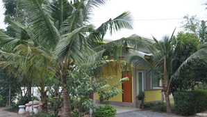 A residential building with a yellow facade, surrounded by lush greenery including palm trees and potted plants. - Feel Good Resort (Nakhon Ratchasima)