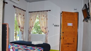 A bedroom with a bed, curtains, a wooden door, and a window. - Feel Good Resort (Nakhon Ratchasima)