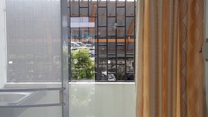 A room with a sliding glass door leading to a balcony, a metal gate, and patterned curtains. - Grand Perfect Apartment (Udon Thani)