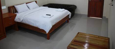 Un dormitorio con una cama de madera, una mesita de noche, un banco de madera, una puerta y un televisor instalado en la pared.