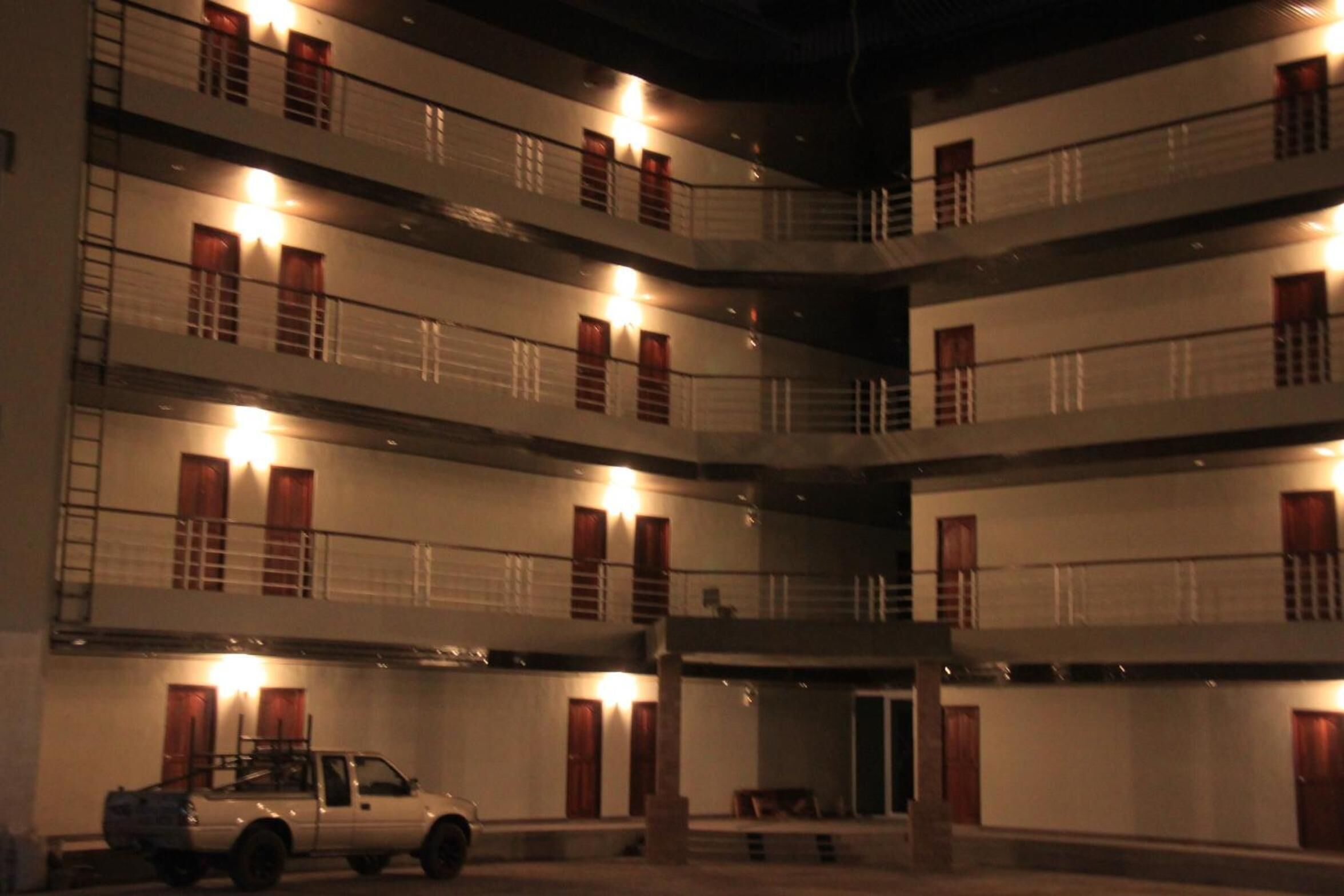A multi-story building with balconies, a parked car, and a door leading to a lower level.