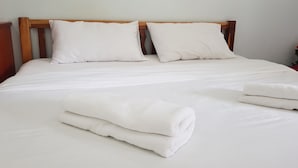 A neatly made bed with white linens and pillows, and two rolled towels on the bed. - Grand Perfect Apartment (Udon Thani)