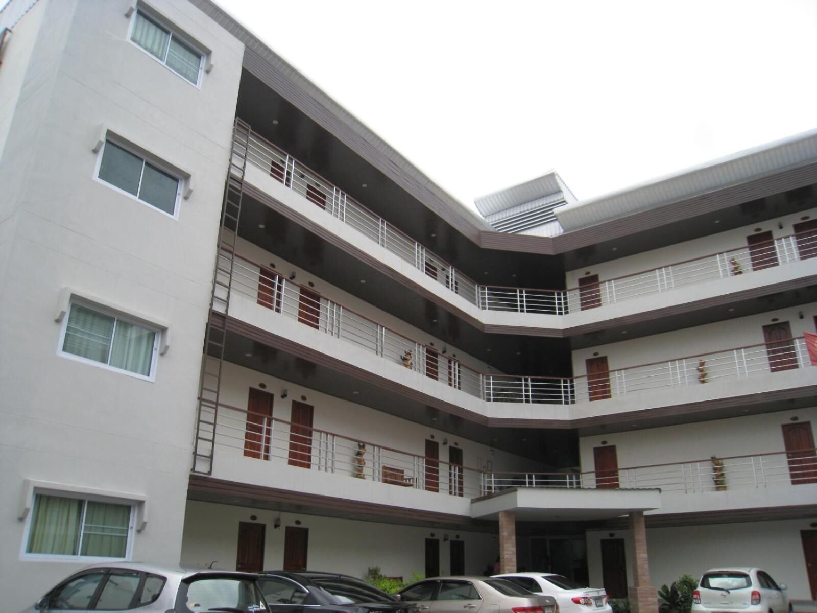 A multi-story building with balconies, a covered parking area, and several cars parked in front.