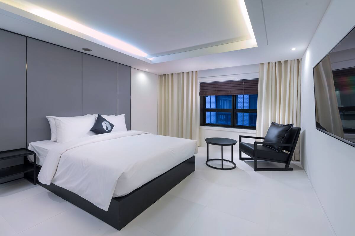 A modern bedroom with a large bed, bedside tables, a small round table, and a chair.