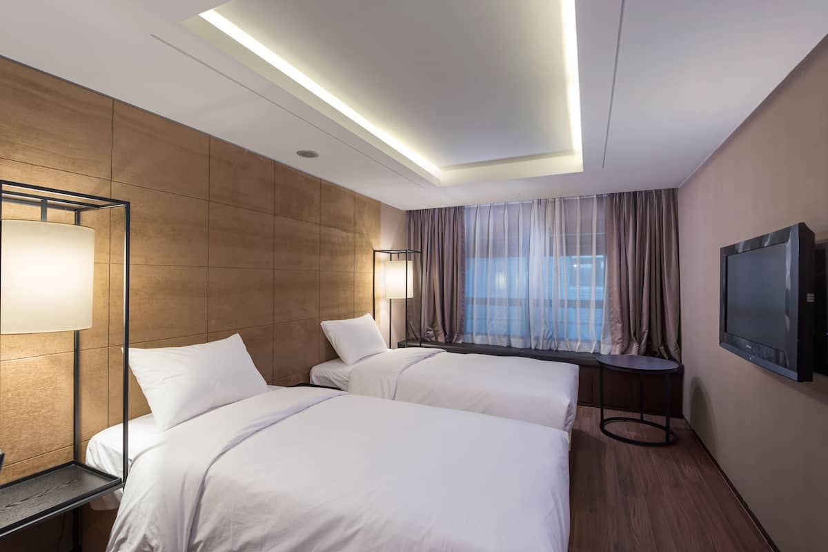 A hotel room with two beds, a TV, a lamp, and a window with curtains.