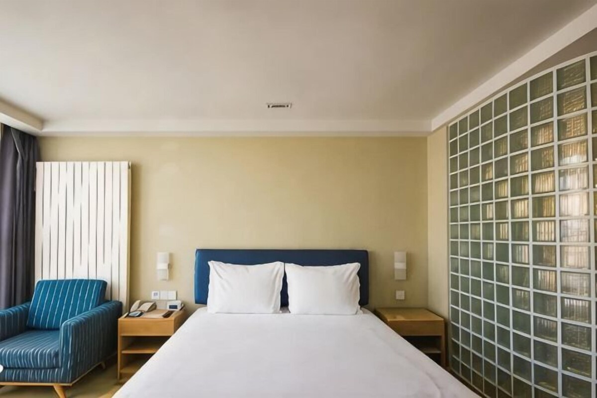 A hotel room with a bed, a chair, a nightstand, and a wall with a grid pattern.