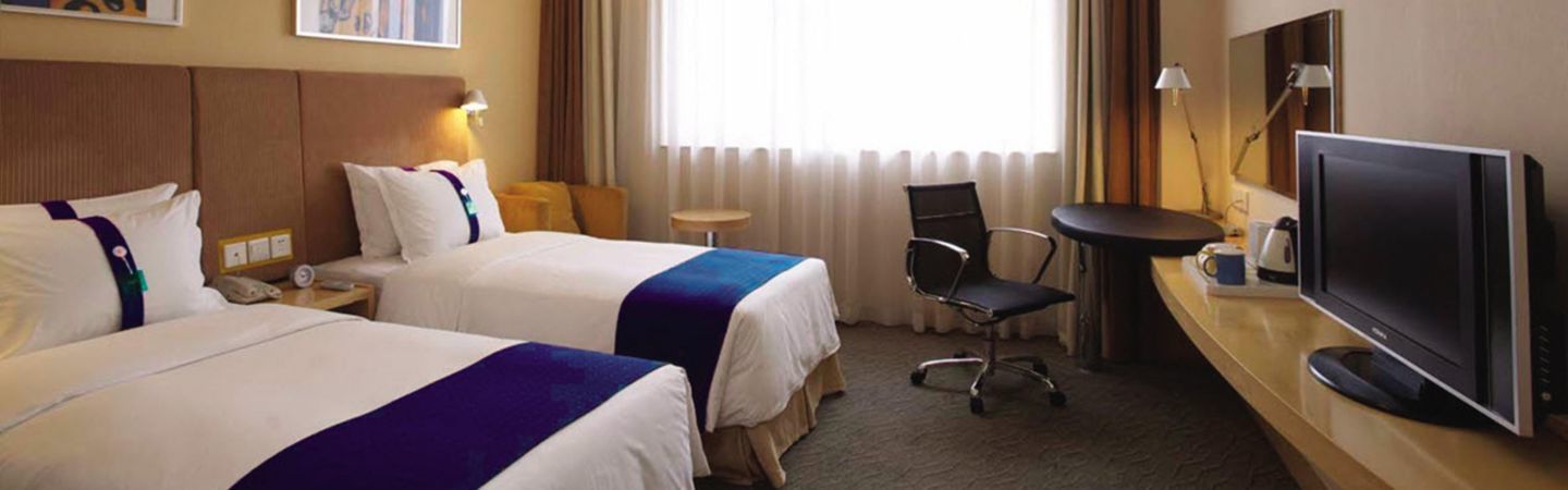 Una habitación de hotel con dos camas, un escritorio con una silla, un televisor y una ventana con cortinas.