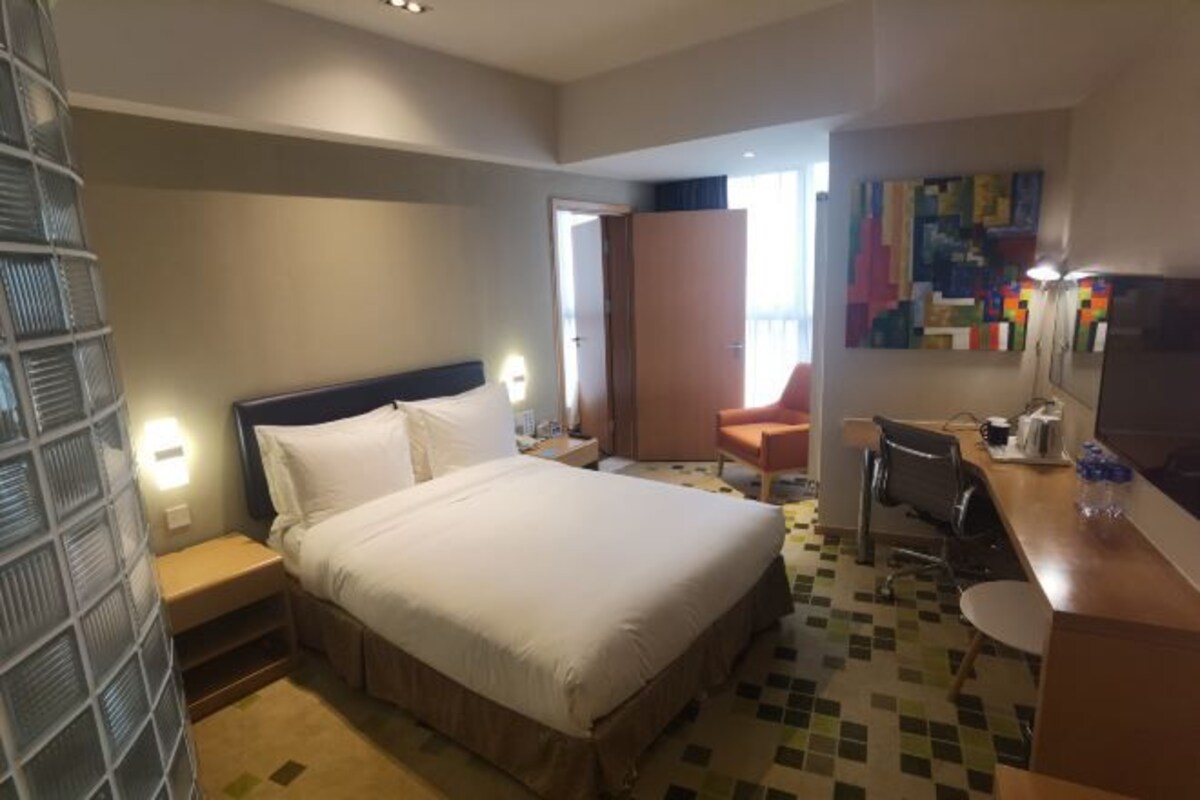 A hotel room with a bed, a desk, a chair, a TV, and a bathroom with a shower and toilet.
