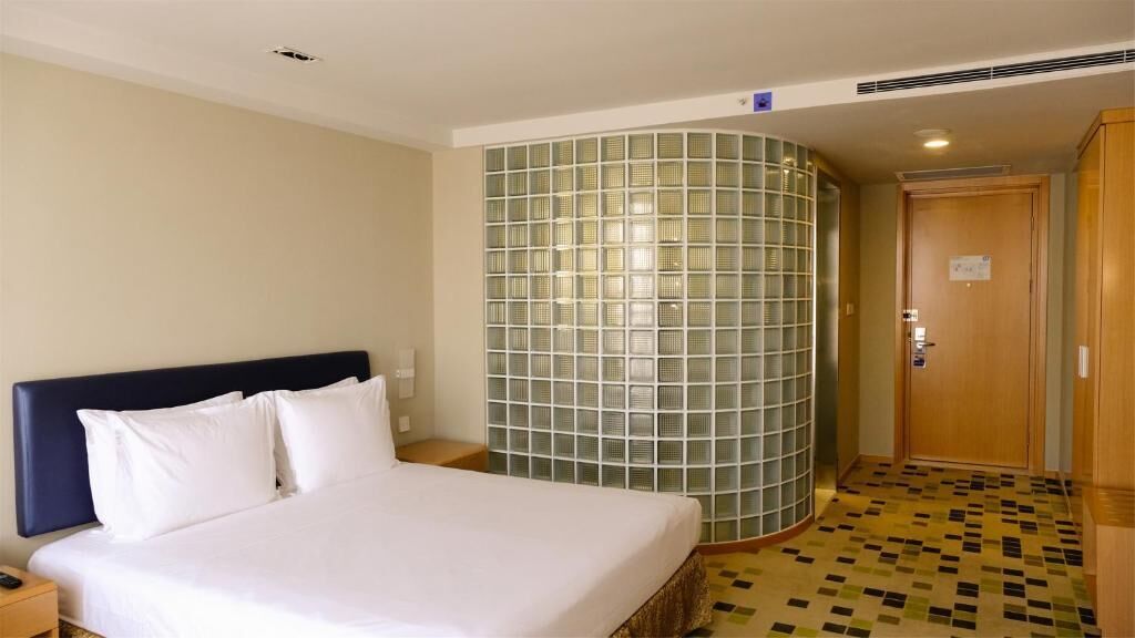 A hotel room with a bed, a nightstand, a wooden wardrobe, a green glass partition, and a tiled floor.