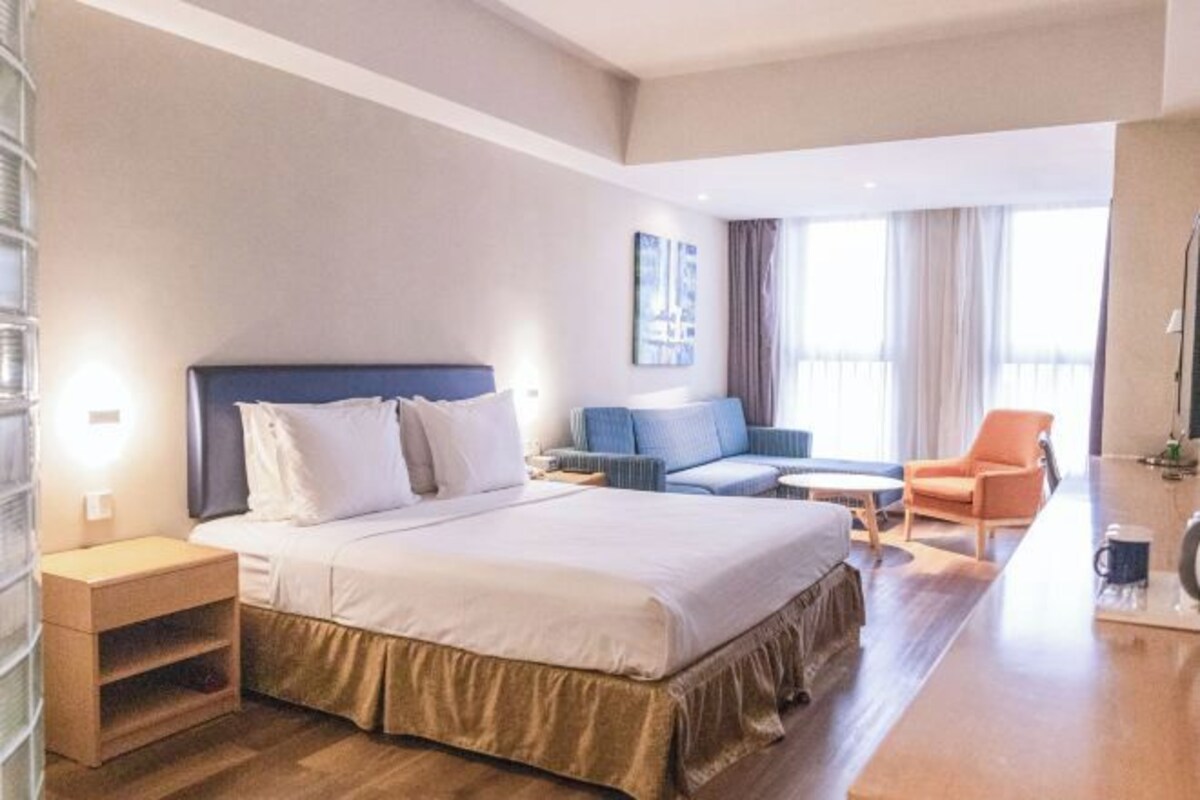A hotel room with a large bed, a sofa, a chair, a small table, and a nightstand.