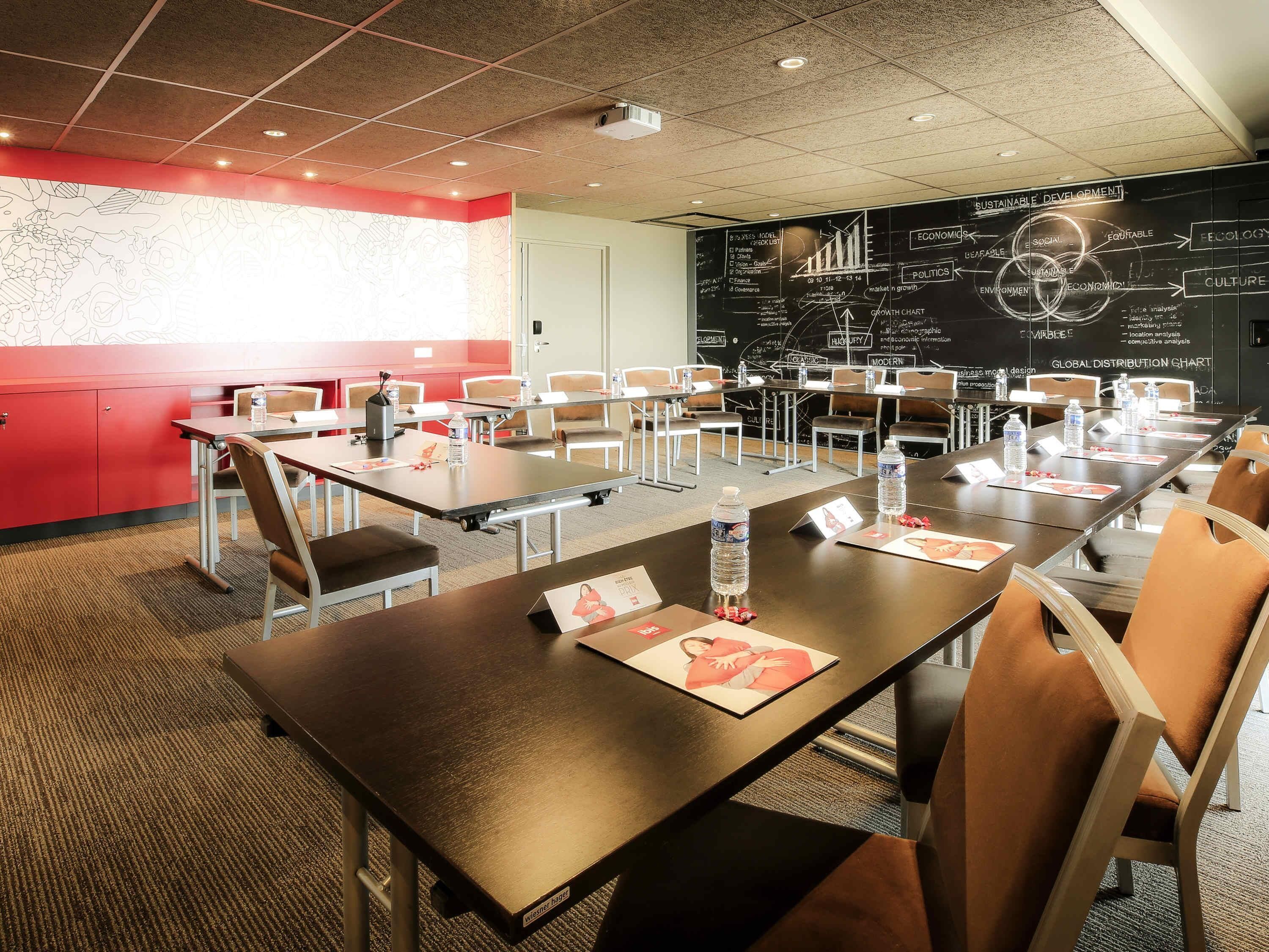 Een vergaderzaal met tafels, stoelen en een schoolbord met diagrammen.