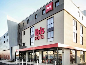 Un hôtel moderne, reconnaissable à son grand panneau « ibis », à ses larges fenêtres et à sa façade plate.