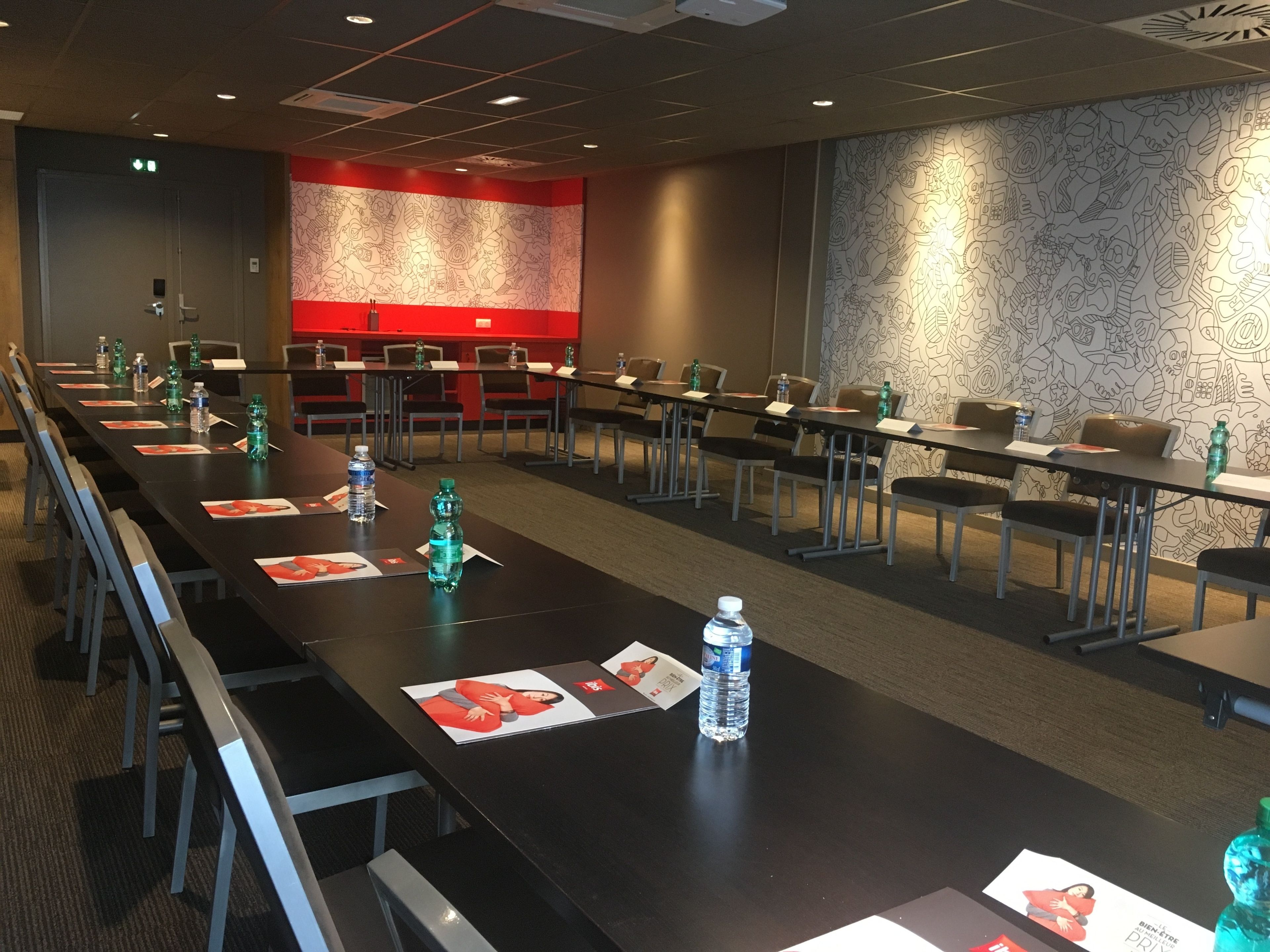 Konferenssihuone, jossa on pitkiä pöytiä, tuoleja, vesipulloja ja nimikortteja.
